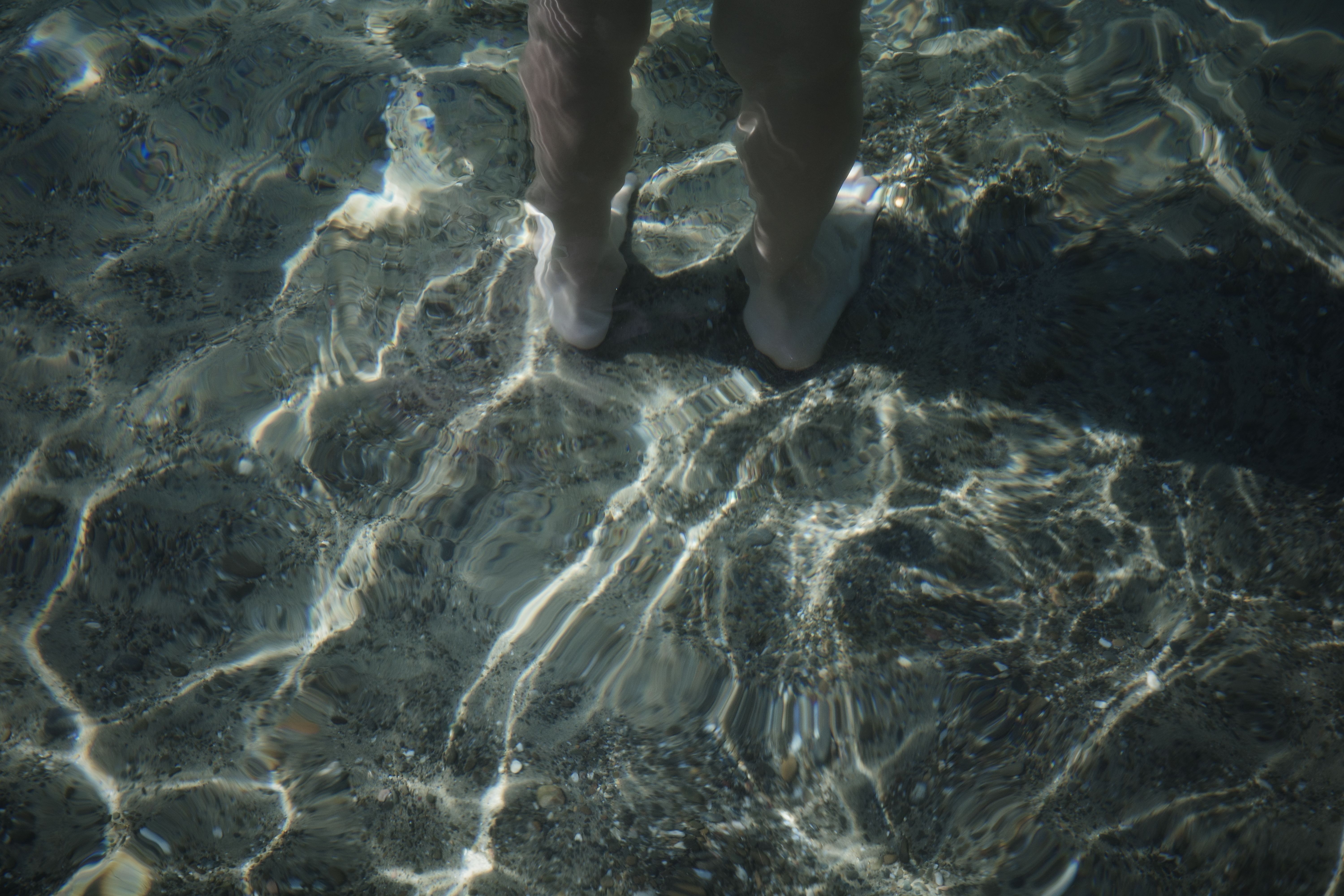 Feet immersed in clear water with sunlight reflections, Congo