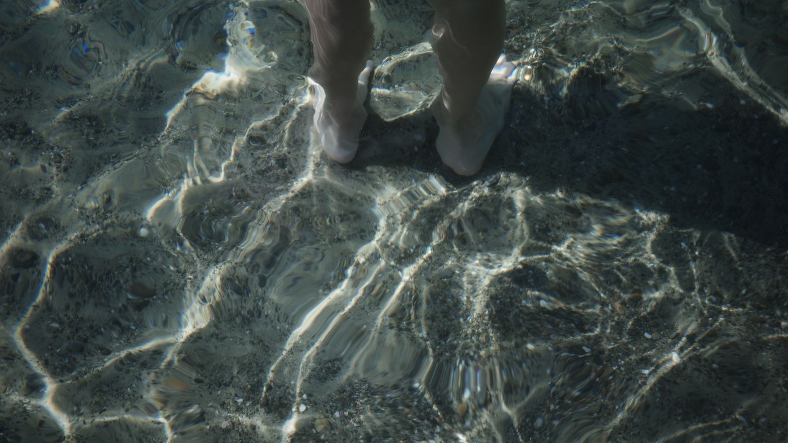 Feet immersed in clear water with sunlight reflections, Congo