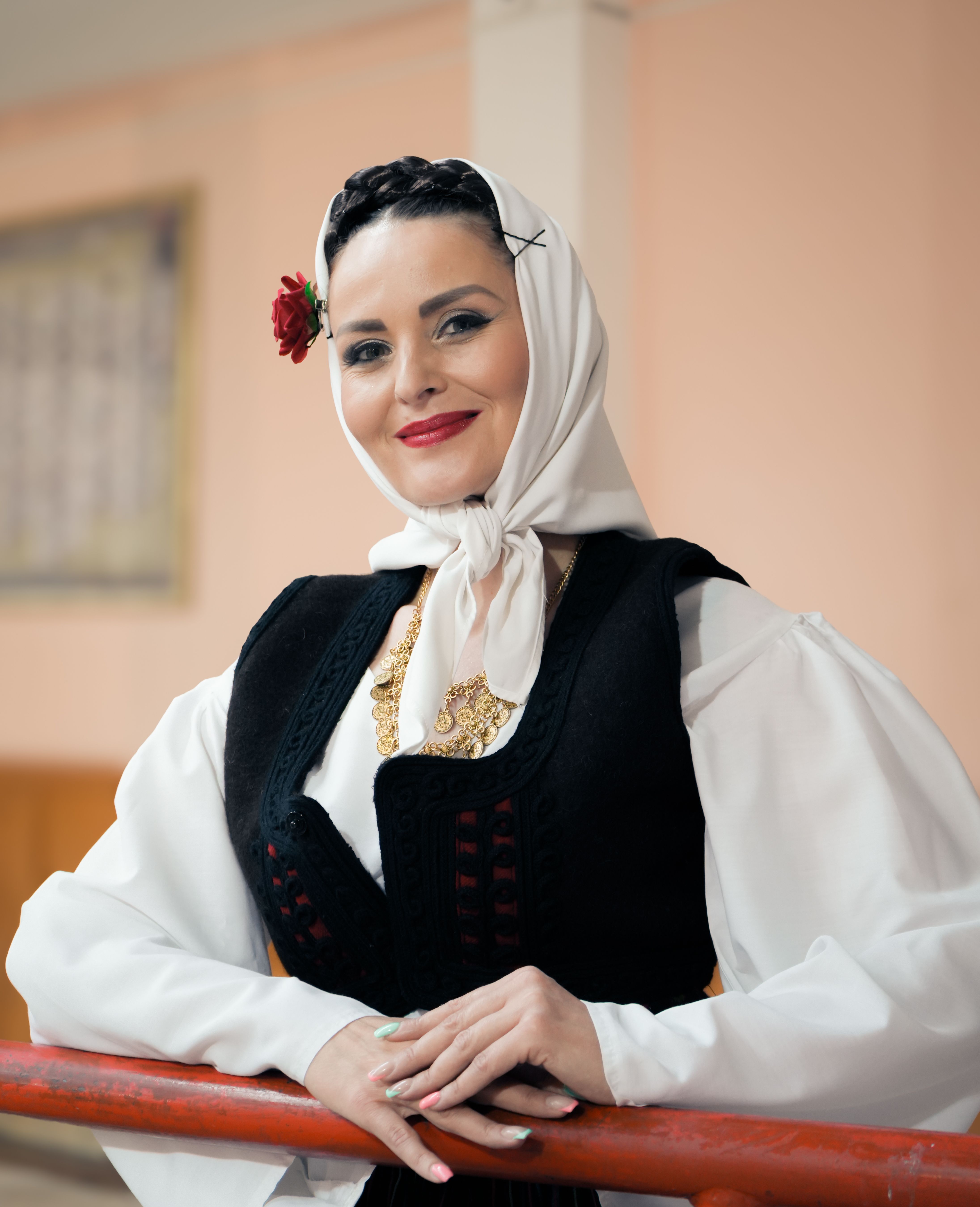 Smiling woman in traditional attire with a headscarf and flower, indoors.