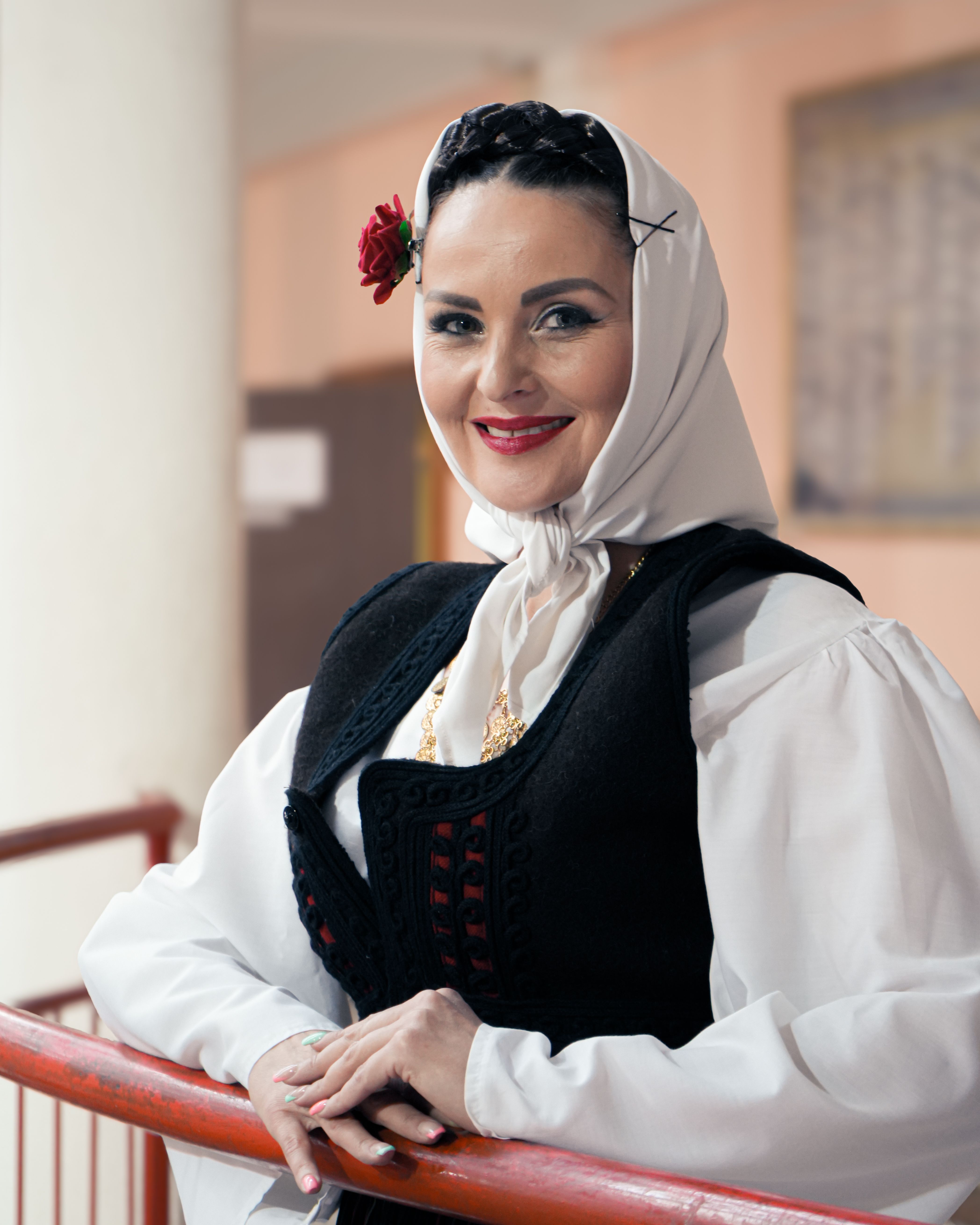 A woman with traditional attire smiles indoors, embodying cultural heritage.