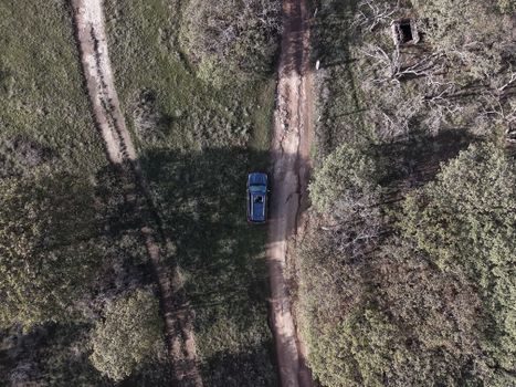 Drone shot of a vehicle on a rural dirt road surrounded by lush greenery.