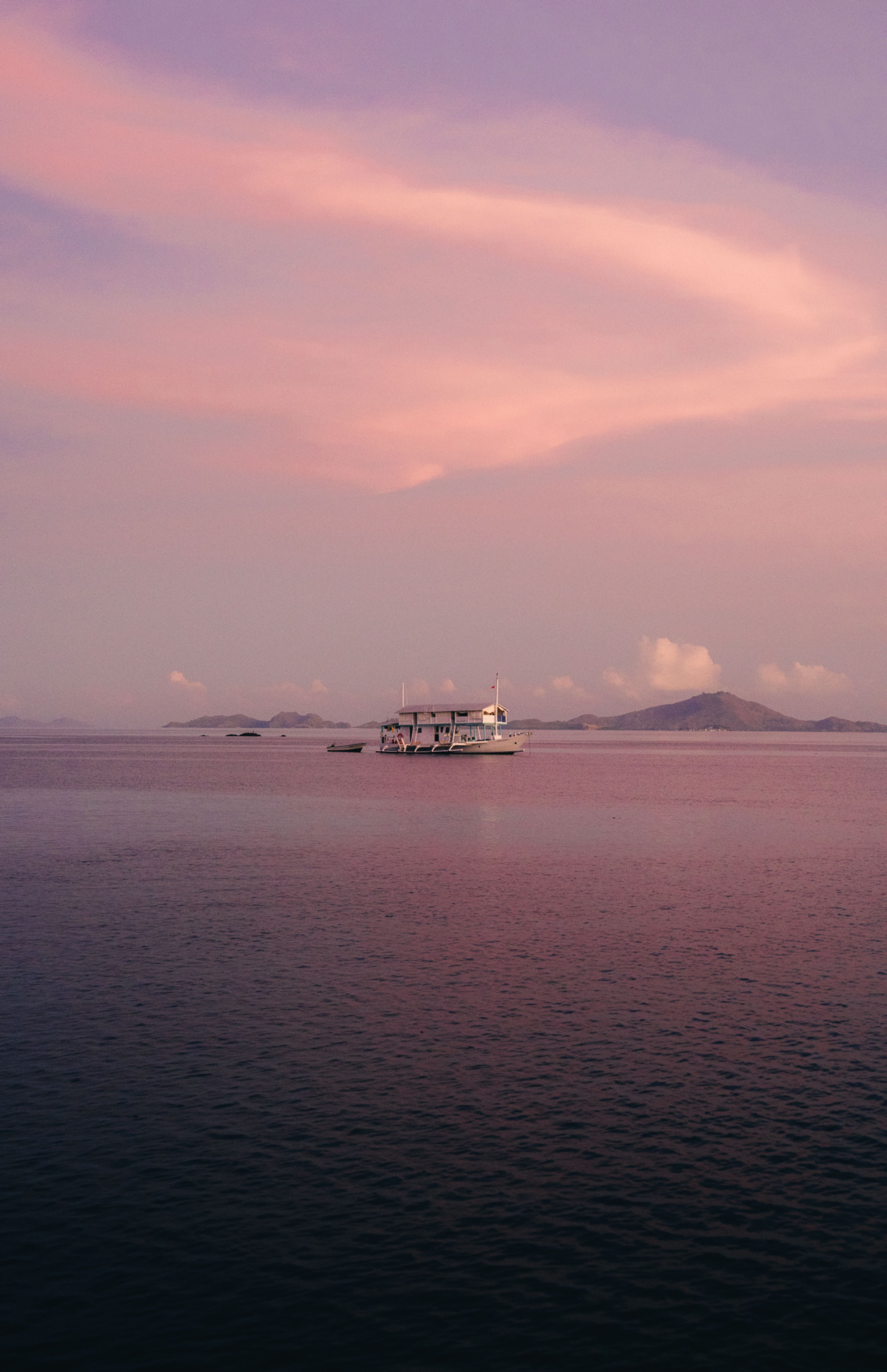 Peaceful sunset view in Bali with a boat on calm waters and pink sky.