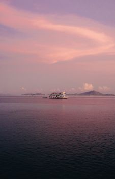 Peaceful sunset view in Bali with a boat on calm waters and pink sky.