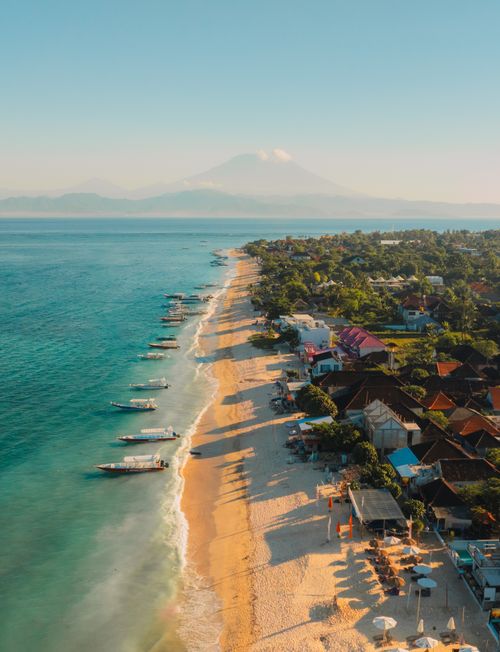 Free Stunning aerial view of Bali's coastline with Mount Agung in the background at sunrise. Stock Photo