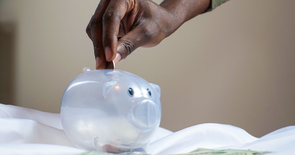 Person putting coin in transparent piggy bank savings account