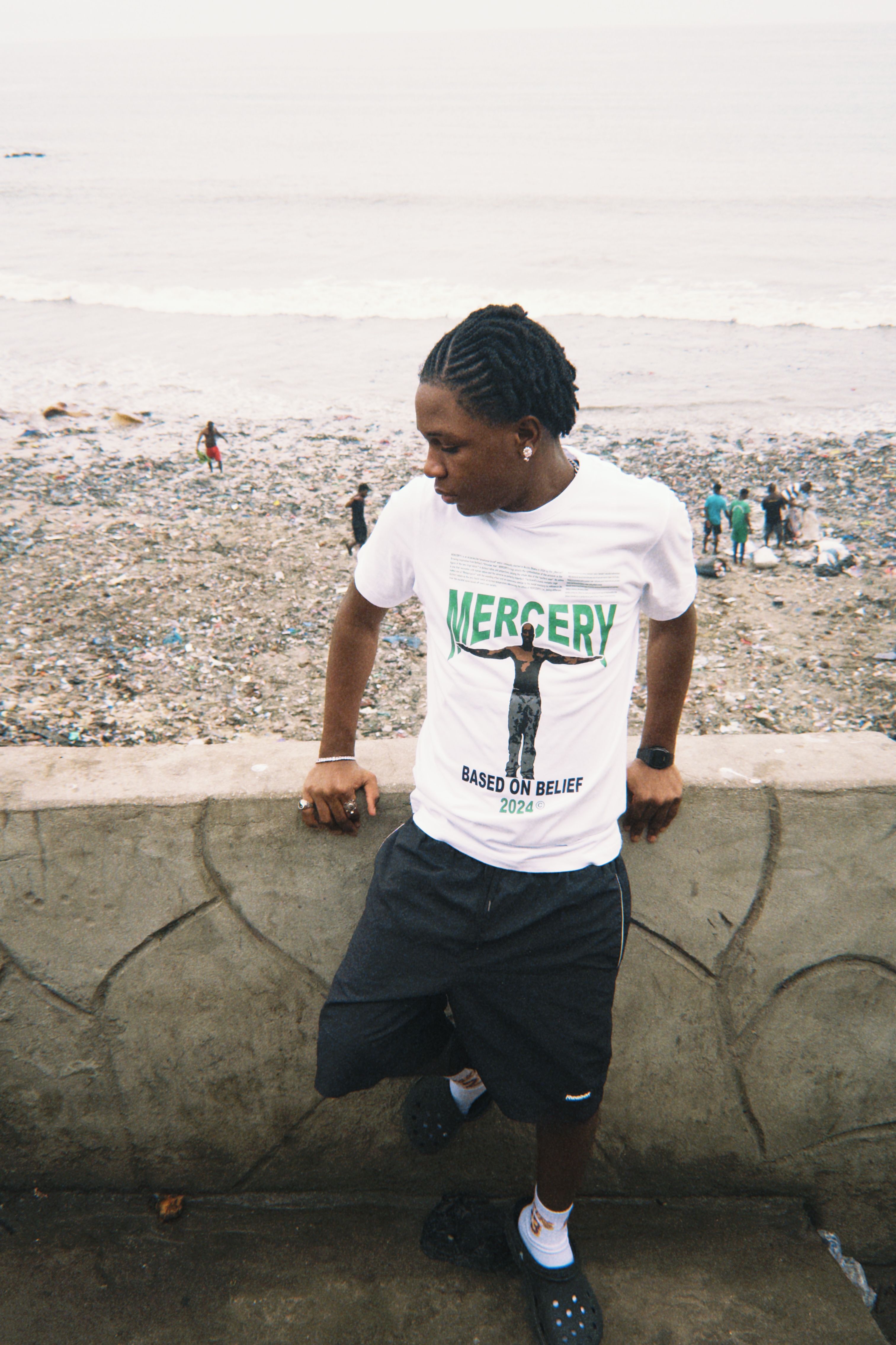 Portrait of a young man leaning on a coastal wall in Ghana, facing the ocean and exuding calm.