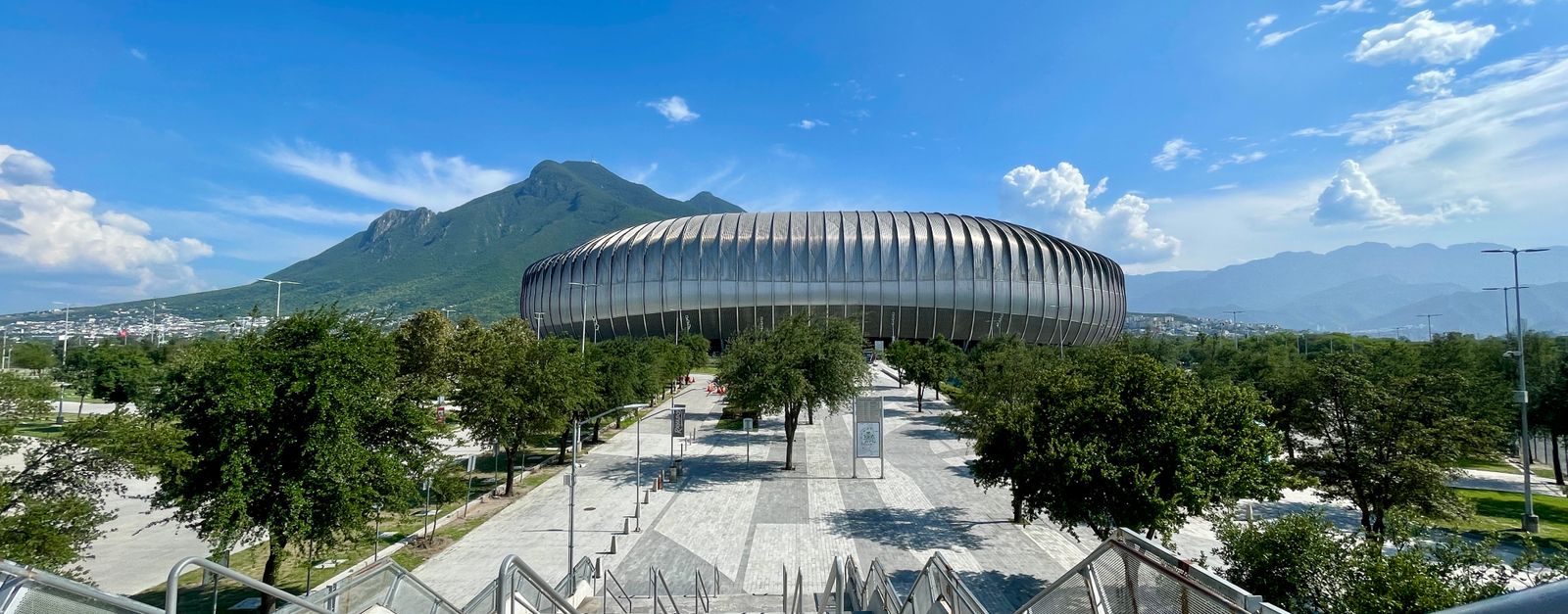 Scenic view of the contemporary stadium against Cerro de la Silla in Monterrey, México, under a bright blue sky.
