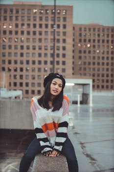 一位时尚女性身着彩色毛衣、头戴帽子，以城市为背景的肖像