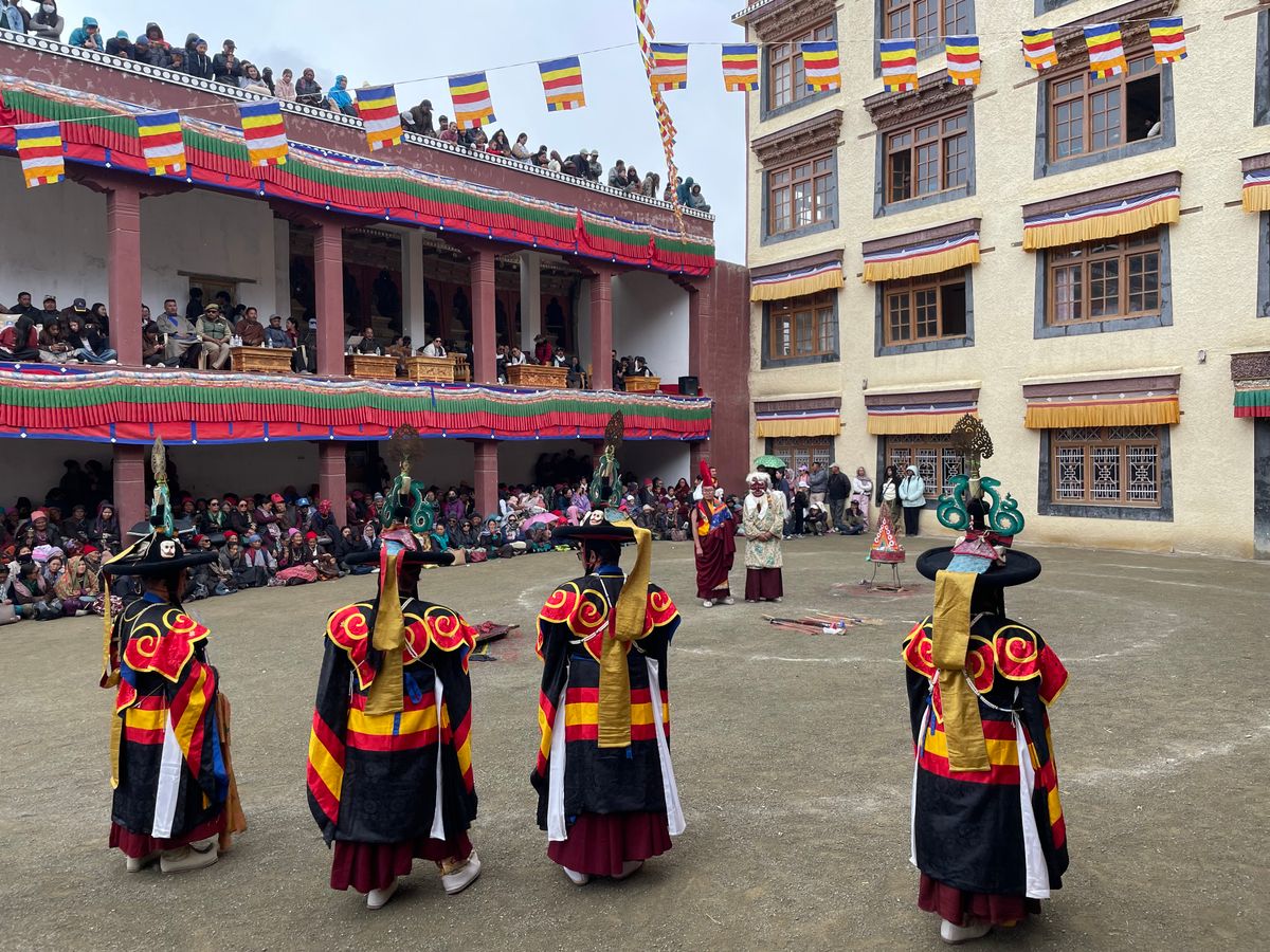 Masked dancers in brocade robes circling a monastery courtyard at the Hemis festival in Ladakh, India