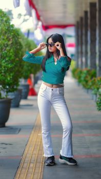 Stylish woman in sunglasses poses confidently on a city street in Bandung, Indonesia, showcasing modern fashion.