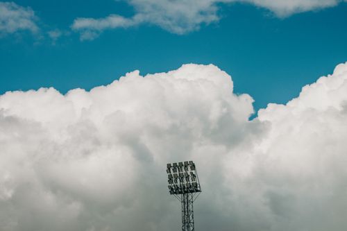 Free Stadium light tower stands against a backdrop of dramatic clouds and vivid blue sky in Jönköping. Stock Photo