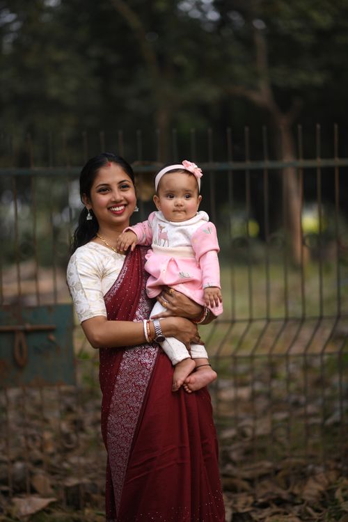 Free A joyful mother in traditional attire holding her baby among trees in a park setting. Stock Photo