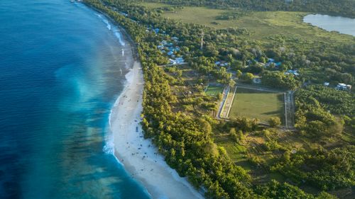 Free Drone shot capturing the tropical beach and lush greenery of Fuvahmulah Island, Maldives. Stock Photo