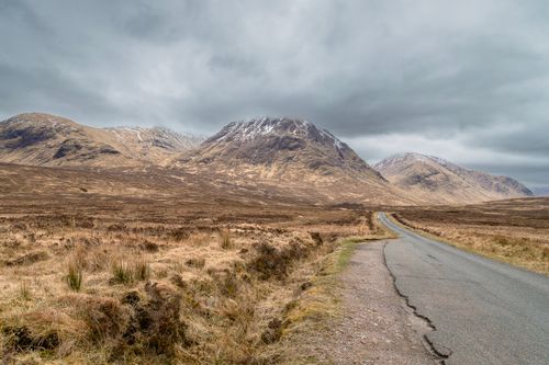 Free Road leading through remote Scottish Highlands with majestic mountains under cloudy skies. Stock Photo