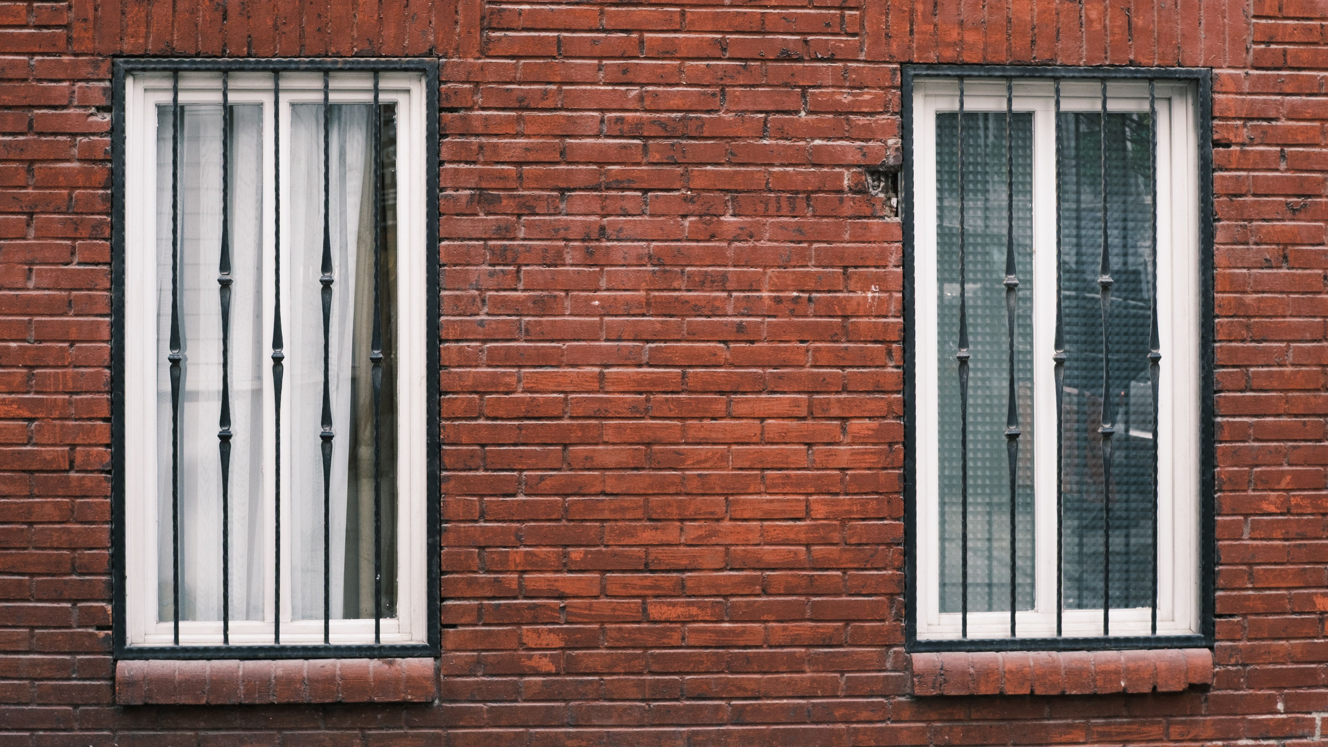 Red brick wall with two barred windows in urban setting.
