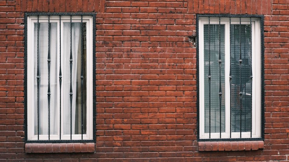 Red brick wall with two barred windows in urban setting.