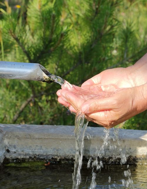 Free Hands catching fresh water from an outdoor pipe, symbolizing purity and refreshment. Stock Photo