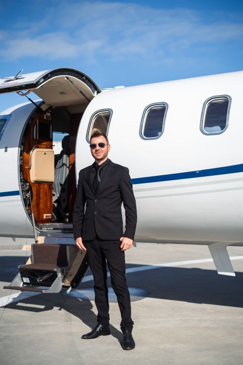 Free Stylish man in black suit poses confidently beside a private jet under clear blue skies. Stock Photo