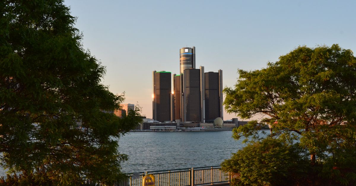 Scenic view of the Detroit Renaissance Center with lush trees framing the skyline at sunset.