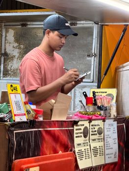 Street vendor taking customer orders at a food stall in Kuala Lumpur, Malaysia.