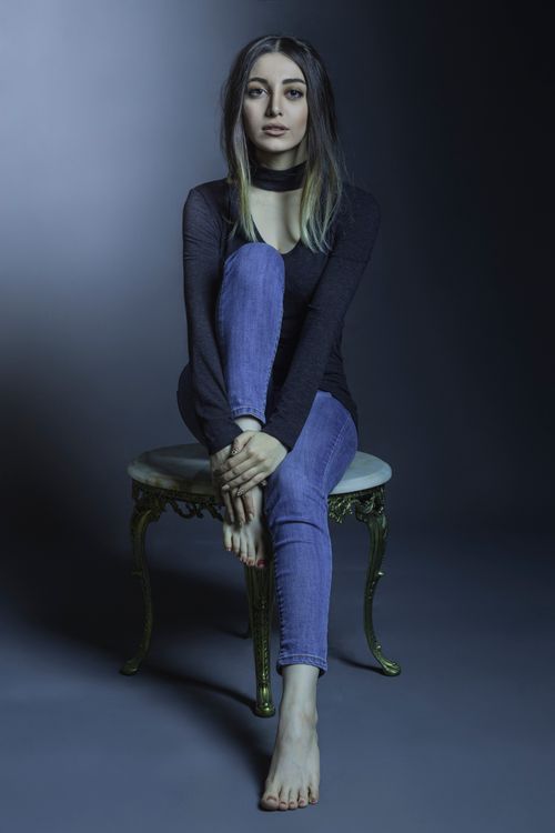 Free Stylish woman in casual wear sitting on a stool in a minimalist studio setting. Stock Photo