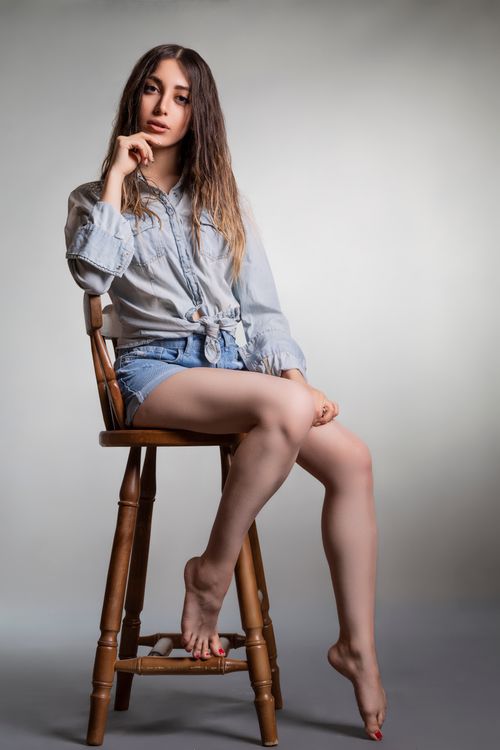 Free Portrait of a trendy young woman sitting on a stool in casual denim attire, exuding modern style. Stock Photo