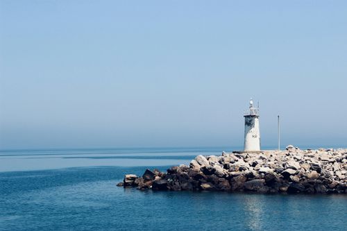 Free A tranquil lighthouse stands on rocky coastline under a clear blue sky, evoking peace. Stock Photo