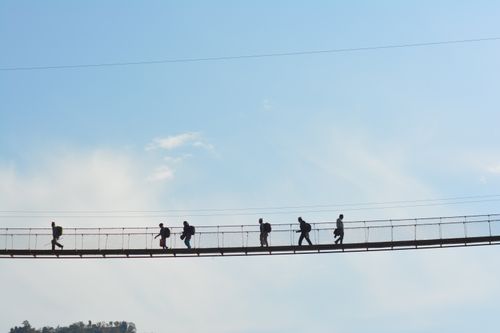 Free A group of people silhouetted against the sky walking across a suspension bridge during the day. Stock Photo