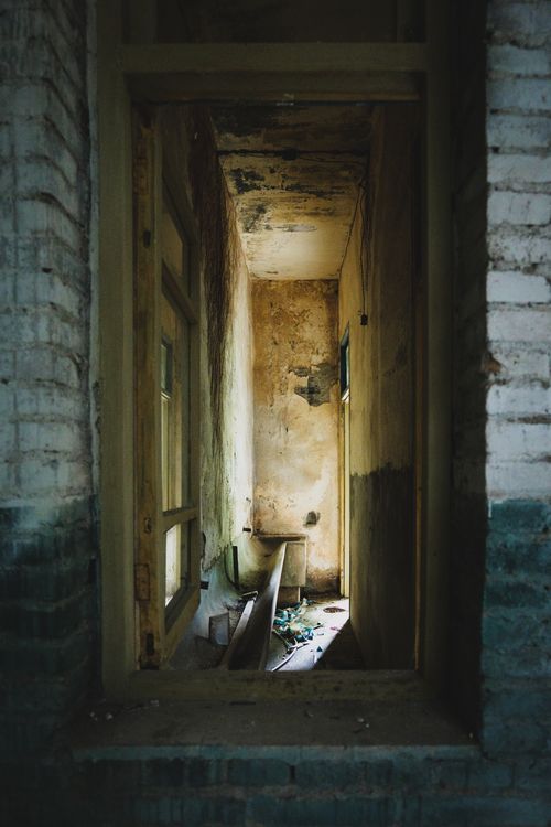 Free View of an abandoned corridor with peeling walls and natural light, creating a mysterious atmosphere. Stock Photo