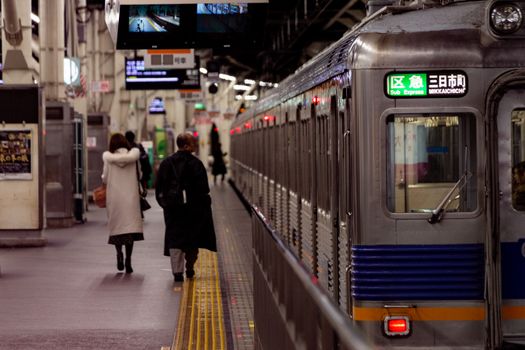 City commuters walking on a platform at Osaka railway station next to an express train.