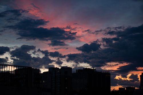 Free A stunning sunset over city buildings with dramatic clouds and vibrant colors in the sky. Stock Photo
