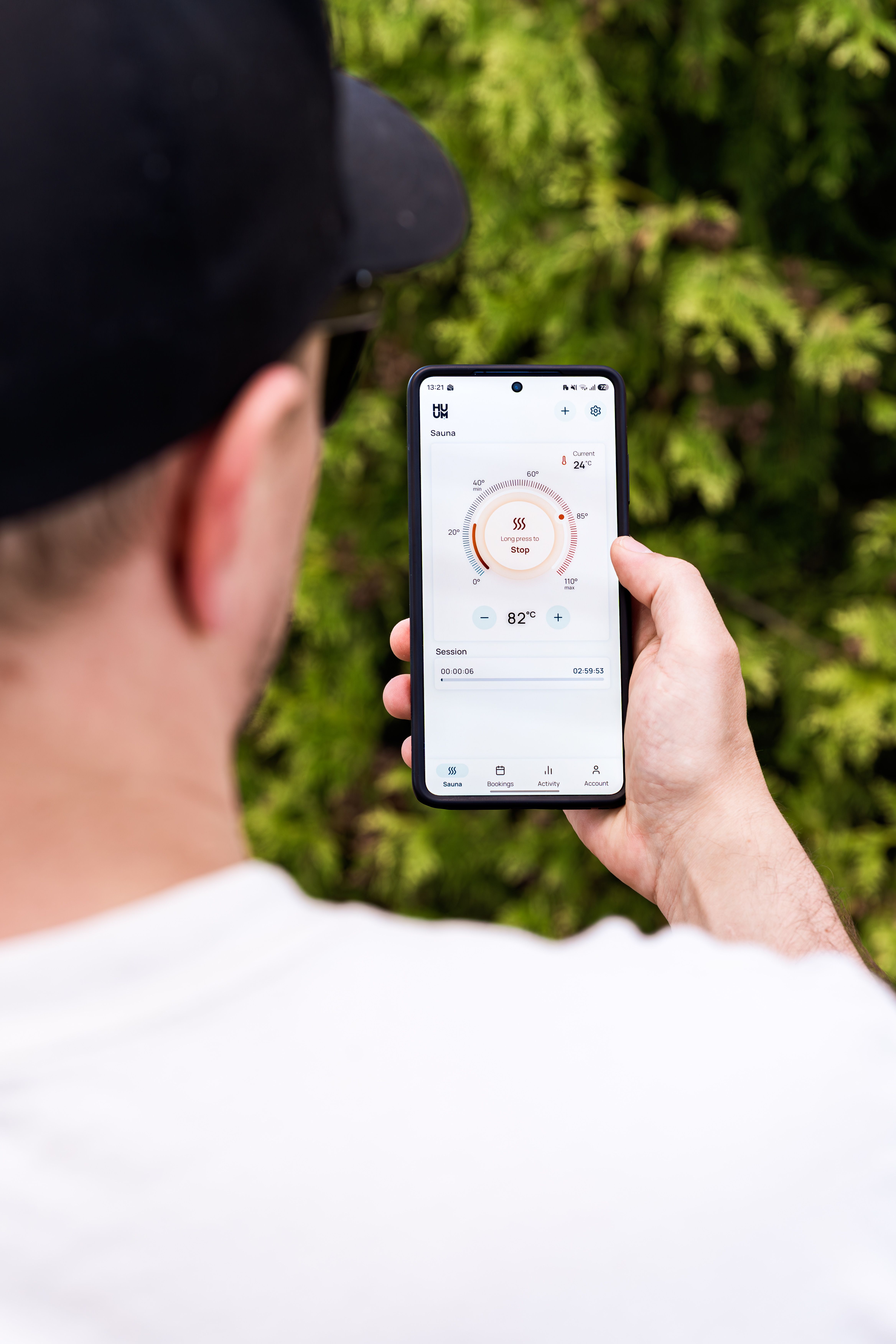 Man holding a smartphone displaying a sauna control app interface, standing outdoors.