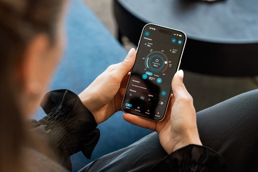 A woman controls a smart sauna system via a touchscreen app on her smartphone indoors.