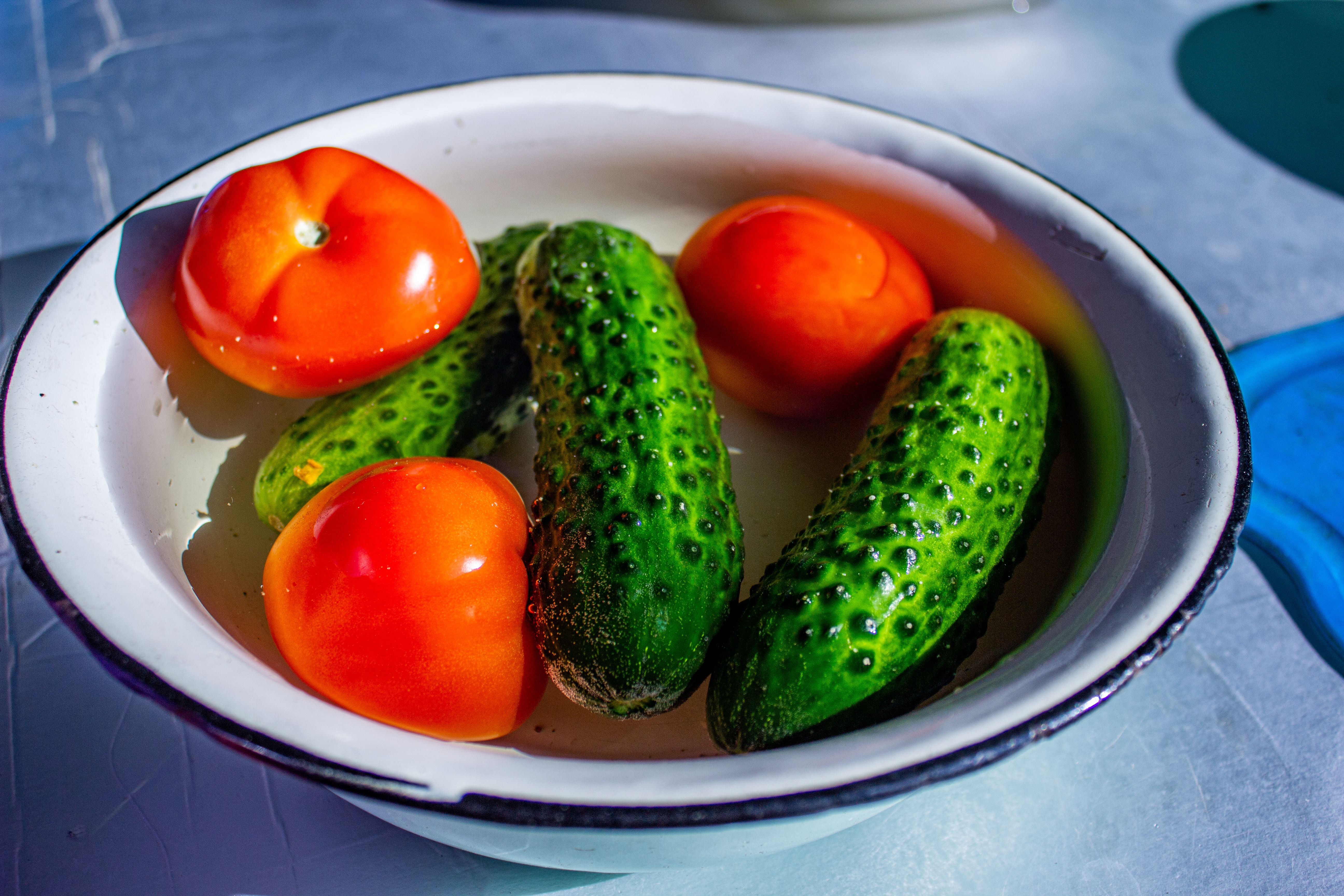 Colorful close-up of fresh tomatoes and cucumbers in a white bowl with vivid lighting.