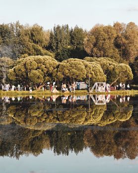 Peaceful lakeside scene with lush trees reflecting on water and people gathered nearby