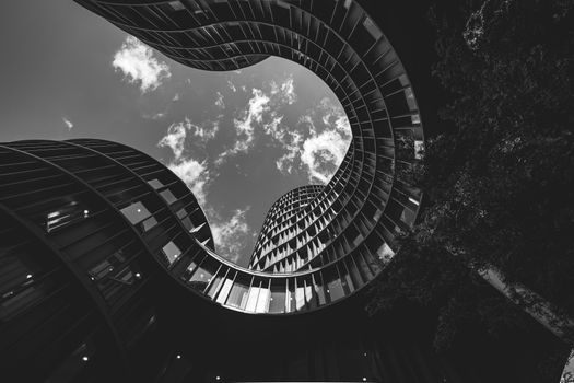 Dynamic view of modern curved architecture captured in monochrome, offering a dramatic perspective of the sky.