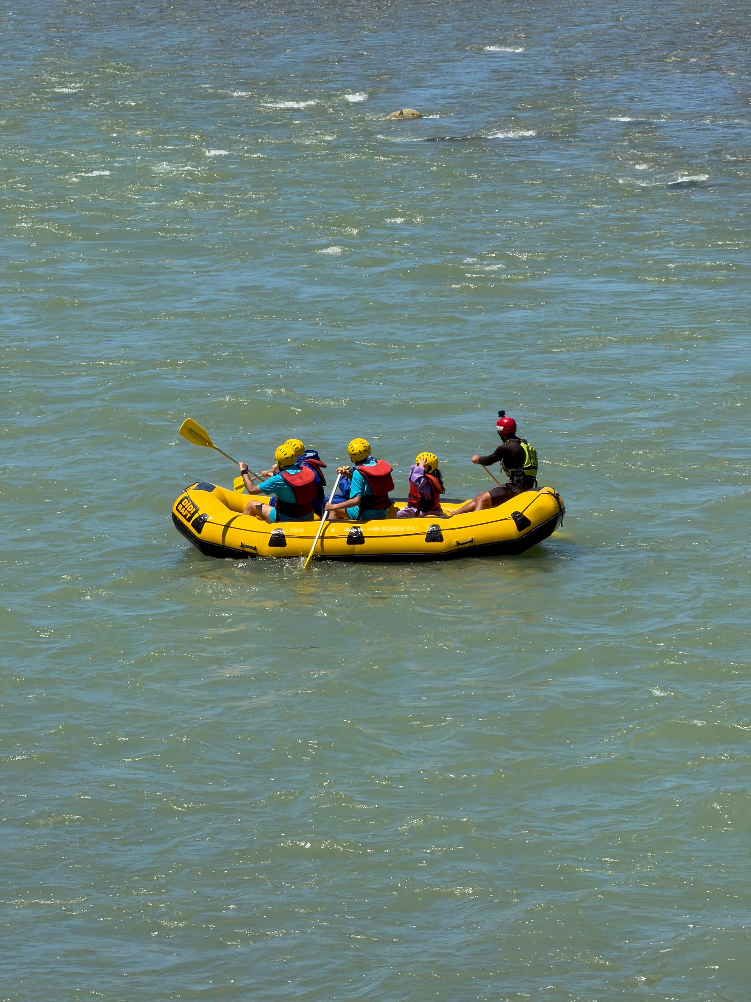 Exciting group rafting adventure on a river in a sunny day setting, featuring a vibrant yellow raft with four participants.