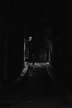 A lone silhouette walking in a dimly lit narrow alley at night, creating a sense of mystery and solitude.