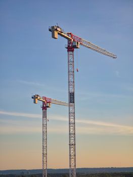 Twin tower cranes rise into a clear blue sky in Oakville, Ontario, Canada.
