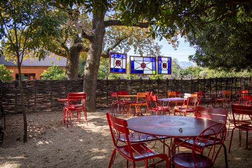 Free Vibrant outdoor cafe with red chairs and stained glass accents under trees, evoking a relaxing garden ambiance. Stock Photo