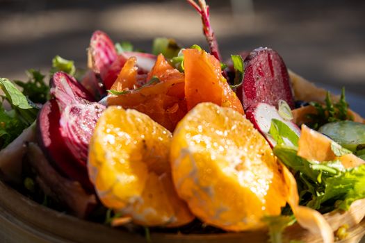 Colorful salad with oranges, beets, carrots, and greens in natural light.