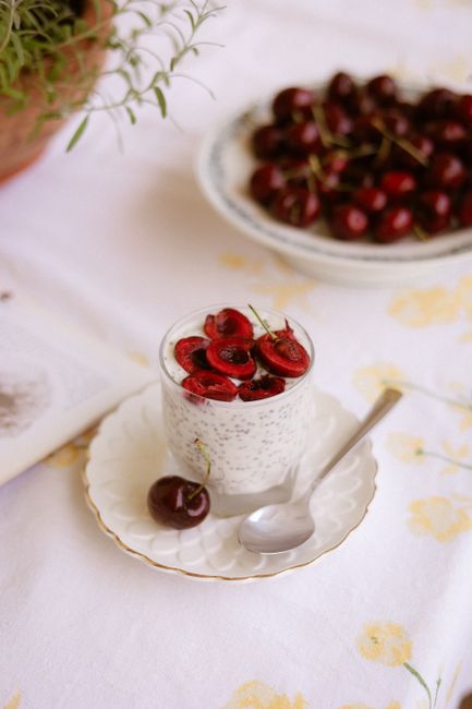 A tall glass of purple-pink chia seed smoothie topped with a sprinkle of whole chia seeds and fresh berries, with a stainless steel straw, next to a small bowl of dry chia seeds.