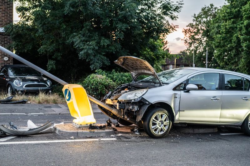 A damaged car that crashed into a lamp post on a London street during twilight.