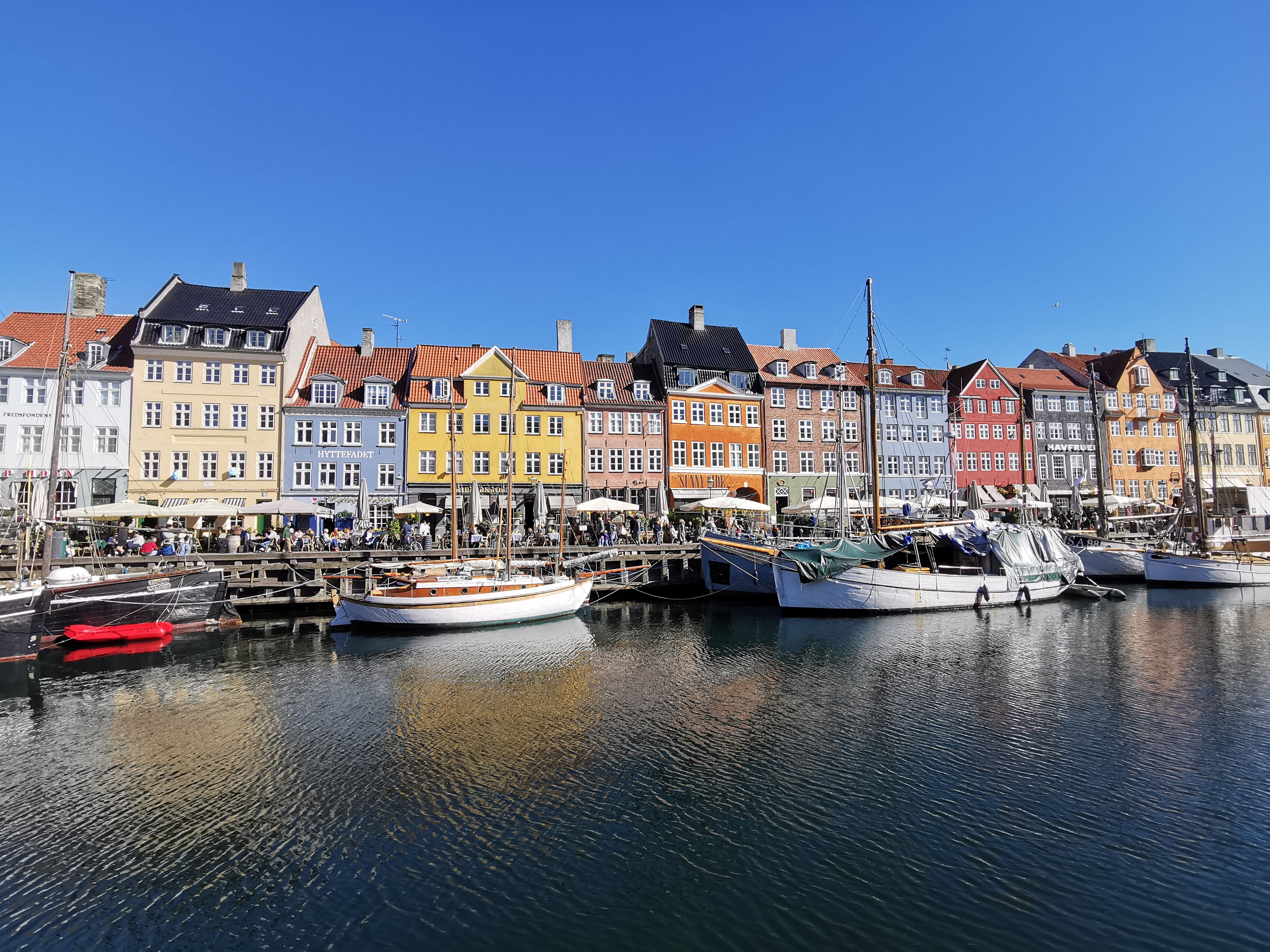 Vibrant Nyhavn harbor with colorful buildings and boats under a clear blue sky in Copenhagen, Denmark.