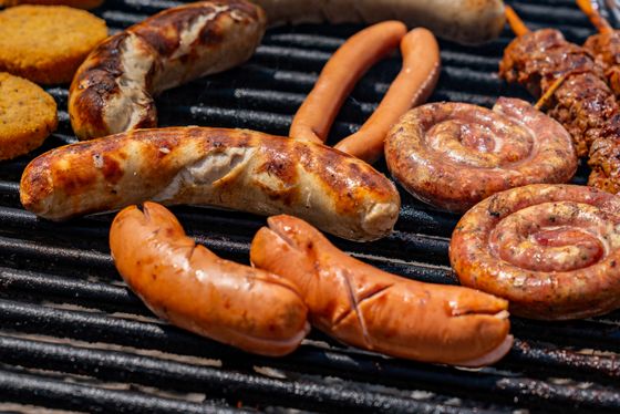 Bratwurst, coiled spiral sausages and scored frankfurters browning on grill grates