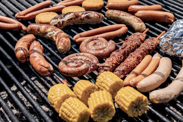 Assorted sausages, spiral sausages, kebabs and corn cobs sizzling on a charcoal grill