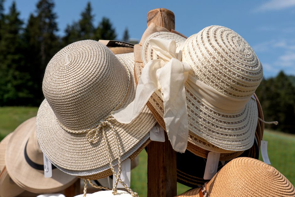 Close-up of stylish sun hats on wooden stand against sunny outdoor backdrop.