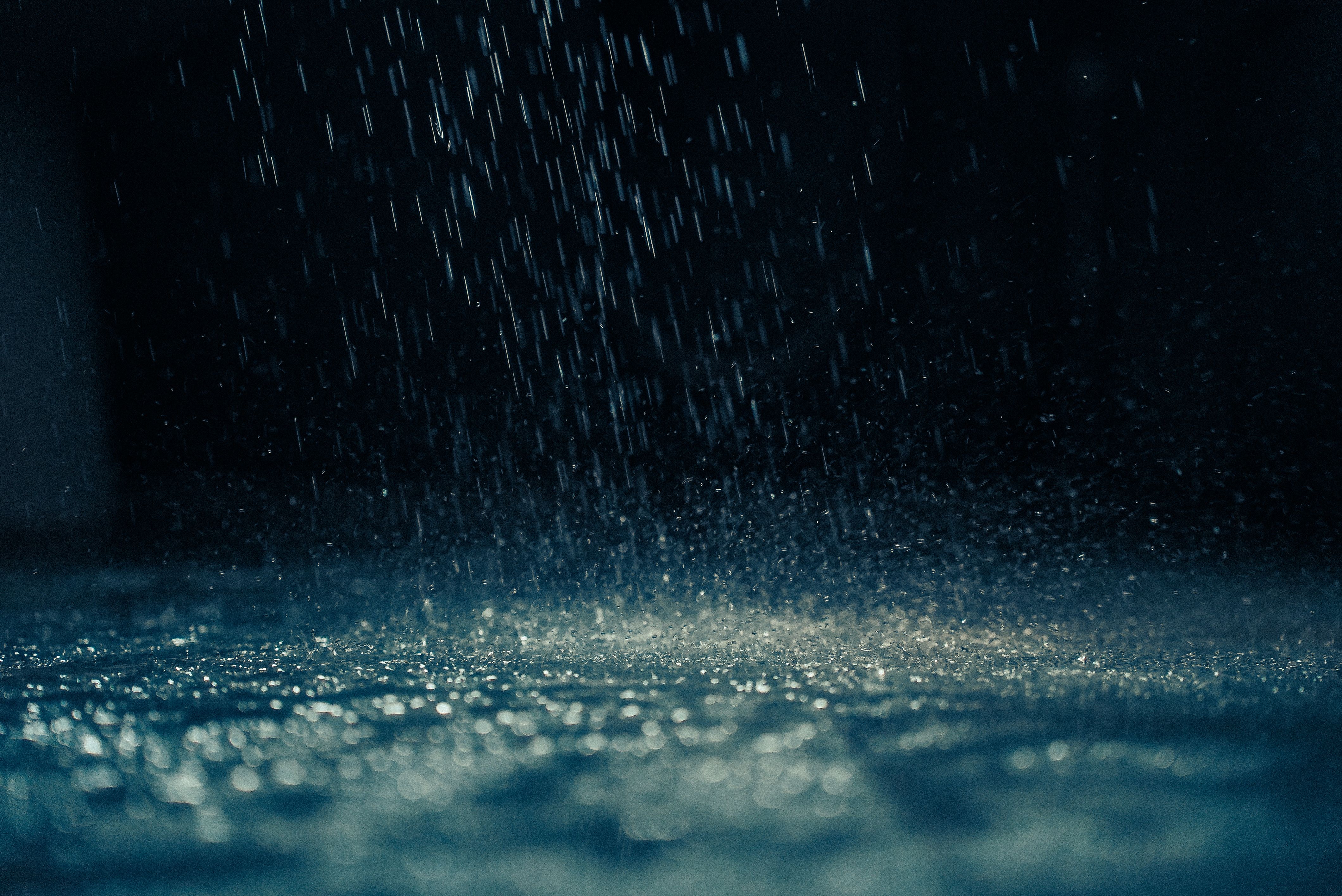 Dramatic close-up of rain droplets falling on a dark surface, capturing movement and reflections.