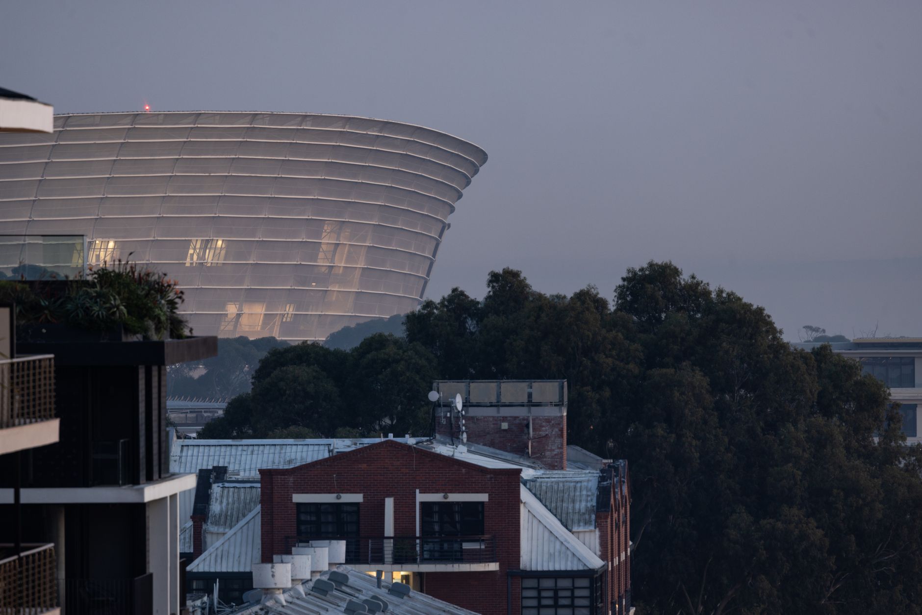 An evening view of Cape Town Stadium with urban buildings in the foreground, showcasing modern architecture in a city setting.