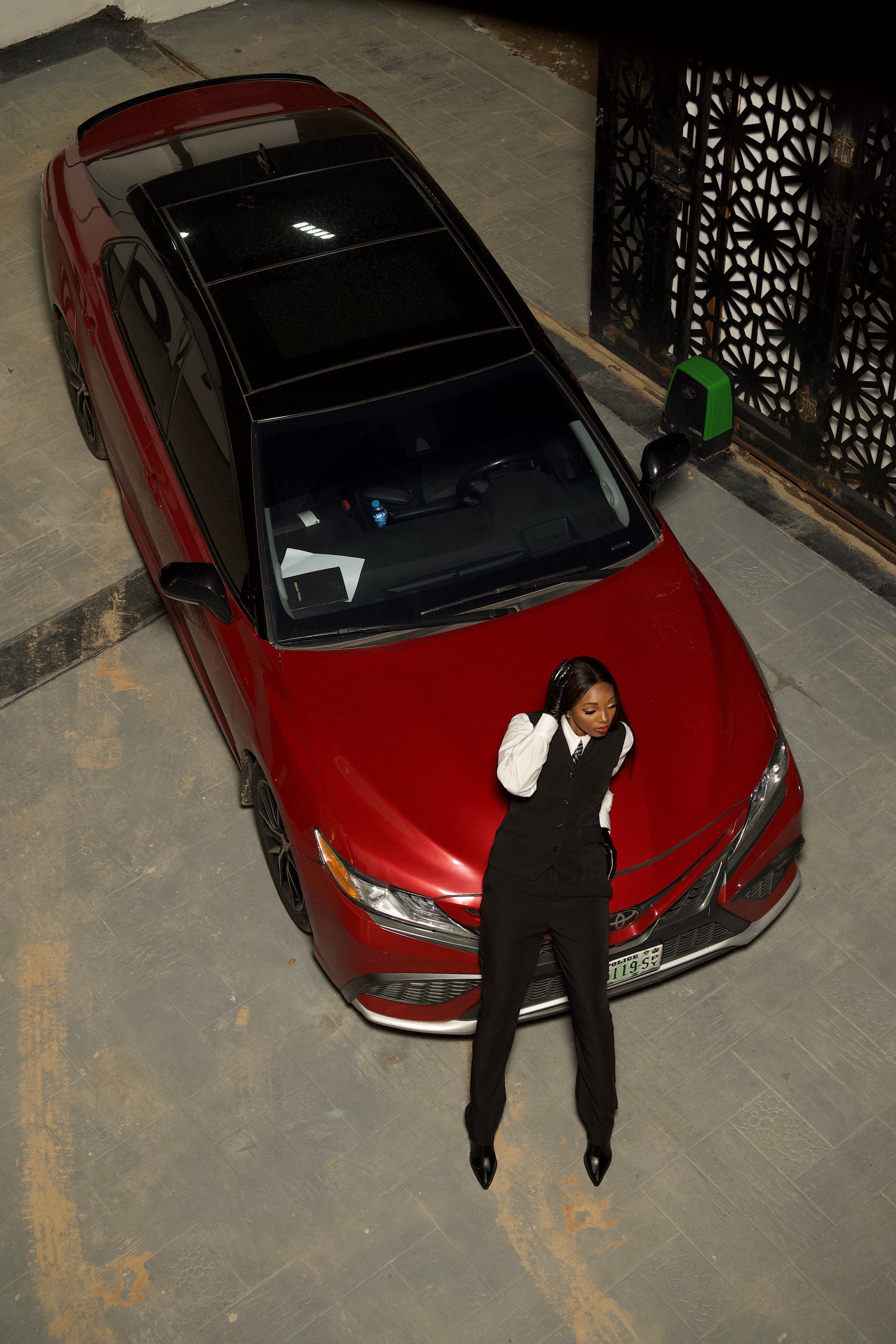 Stylish Woman Posing on Red Car in Urban Setting